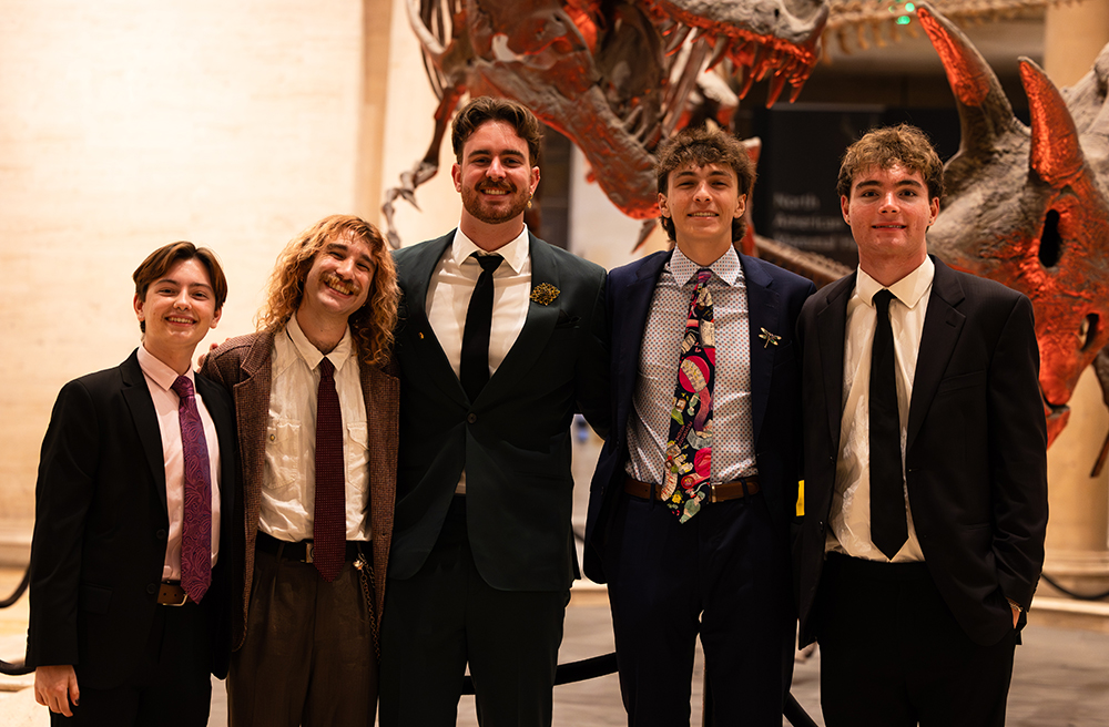 AXS members Evan MacIntosh, Red Stone, Ethan Hery, Karchy Borsa, and Felix Burkhart pose by the T. Rex fossils. 
